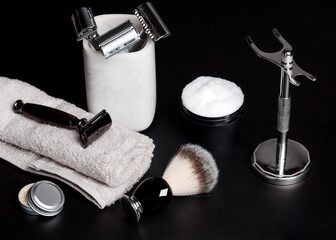 Razor and brush on stand, towels, perfume, balsam and blades on a black background.