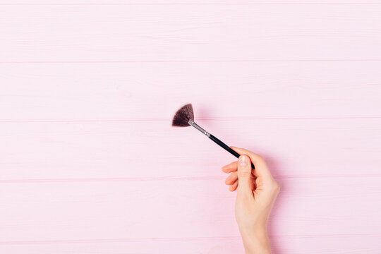 Female Hand Holding Makeup Fan Brush On Pink Background