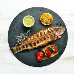 Grilled trout with vegetables on a black plate. Top view. free space for your text. Rustic style.