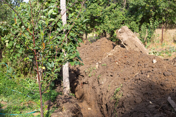 A ditch dug by an excavator in the ground in a village for laying a water supply system. Residential water supply