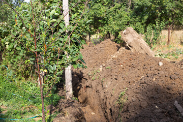 Fototapeta na wymiar A ditch dug by an excavator in the ground in a village for laying a water supply system. Residential water supply