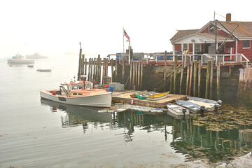 Fototapeta na wymiar Foggy morning in coastal Maine. Lobster boat docked alongside wharf on Spruce Head Island. American flag flying.