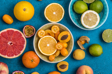 Variety of tropical colorful summer fruits in bowls and on blue background, some of the citrus fruits cut in half