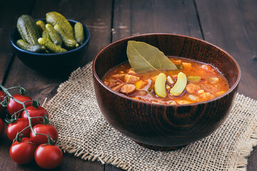 Bowl with Solyanka, a spicy and sour soup of Russian origin, on dark wooden table. Soljanka is...