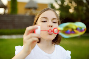Pretty teenage girl blowing soap bubbles on a sunset. Child having fun in a park in summer.