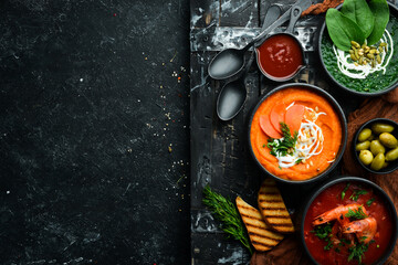 Three bowls with colored soup. Spinach, tomato and carrot soup. Healthy food. On a dark background.