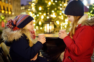 Two adorable sisters drinking hot chocolate on traditional Christmas fair in Riga, Latvia. Children...