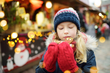 Cute young girl having gingerbread cookie on traditional Christmas fair in Riga, Latvia. Child enjoying sweets, candies and gingerbread on Xmas market.