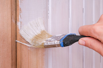 Wooden house renewal, a hand repainting a plank wall into a white color using a paintbrush and...