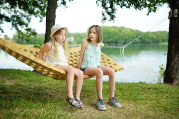 Cute young sisters having fun in hammock on beautiful summer day. Children relaxing in summer park.