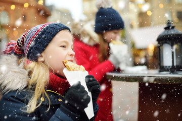 Cute young girls eating crepe pancake on traditional Christmas fair in Vilnius, Lithuania. Children...