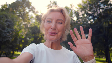 Happy senior woman relaxing in park talking on video call with family