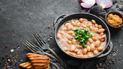 Boiled beans with parsley in a black plate. Top view. Free space for your text. Rustic style.