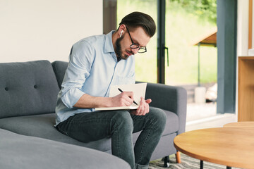 Bearded man writing with pen in his notebook. Working from home office