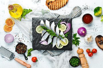 Salted herring with onion and lemon on a black stone board. Top view. Free space for your text.