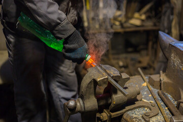 Professional blacksmith working with metal - quenching hot iron part with water at forge, workshop....