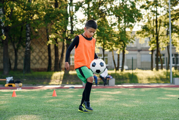 Motivated hispanic teen football player stuffs soccer ball on leg. Practicing sport exercises at...