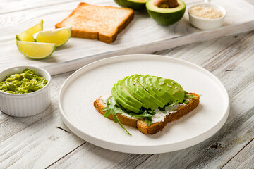 Toast with avocado, cream cheese,guacamole and arugula on white wooden table