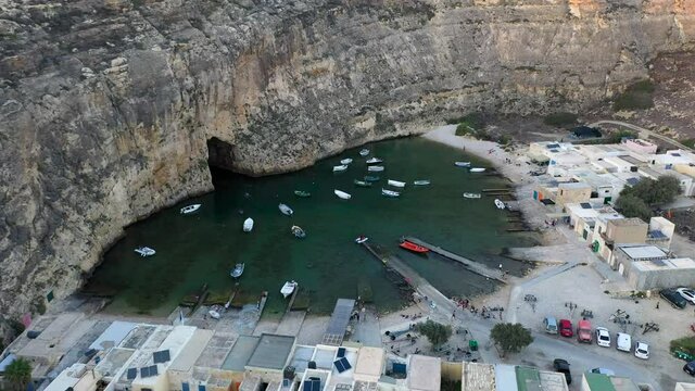 Drone ascends over Maltas Inland Sea Cave with Powerboats and Sail boats siting anchored in Turquoise Clear Calm Water