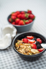 Healthy breakfast Granola with strawberries, banana, nuts and blackberries stands on the table. Ingredients in the background.