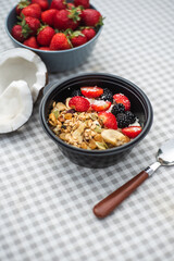 Healthy breakfast Granola with strawberries, banana, nuts and blackberries stands on the table. Ingredients in the background.