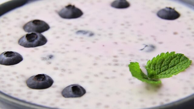 Rotating of yogurt with blueberry and chia in ceramic bowl on white background. Side view, close up.