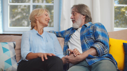 Happy senior couple talking while sitting on couch in cozy home interior