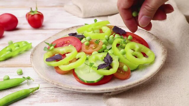 Vegetarian salad from, tomatoes, pepper and basil on white wooden background and linen textile decorating with pea seeds. Side view, close up.