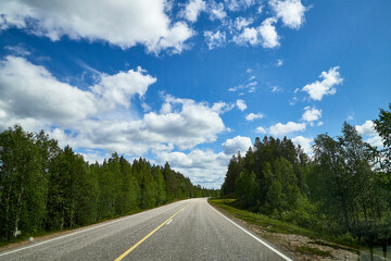 View from relief car windscreen on the blue sky with white clouds, grey asphalt road and landscape with forest and green teeses. Landscape through window