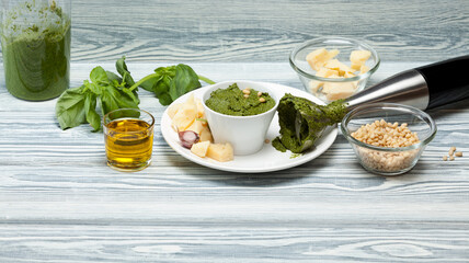 Traditional Italian pesto sauce made from fresh Basil leaves with pine nuts, Parmesan cheese and olive oil using a blender. Wooden table, selective focus, copy space