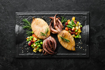 Baked squid with vegetables in a black stone plate. Seafood. Top view. Free space for your text.