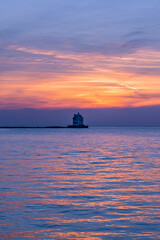Naklejka na ściany i meble Historic lighthouse in calm water of bay under beautiful sunset