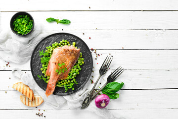Baked sea red perch with green peas on a black stone plate. Top view. Free copy space.