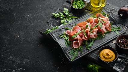 Jamon and arugula on a black stone plate. Prosciutto. Top view. Free space for text.