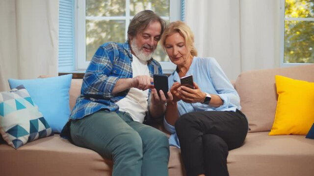 Happy mature couple relaxing on couch and surfing internet on mobile phone