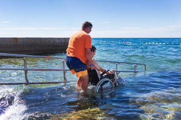 Accessible beach with ramp for disabled people. Man on wheelchair going swimming.