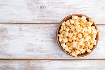 Popcorn with caramel in wooden bowl on a white wooden background. Top view, copy space.