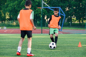 Two motivated teen football players passes soccer ball each other on the football stadium during training exercises.