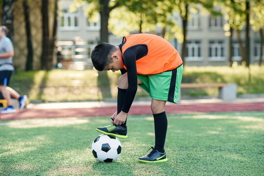 Close up young football player which puts his leg on ball and tying shoelace on soccer stadium during the training.