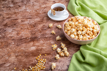 Popcorn with caramel in ceramic bowl on brown concrete background. Side view, copy space.