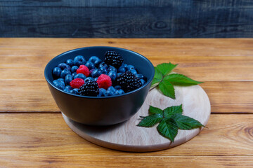 blueberry berry in dark gray ceramic bowl on dark blue wooden background.