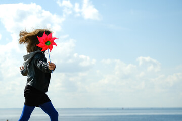 Happy child with red wind spinner on sky urban background.