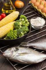 Raw fish with vegetables on grill grate. Egg and  flour, bottle with oil.