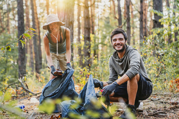 Portrait of young man and woman picking up trash from forest with look in camera