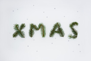 Word Xmas made of spruce branches and decorated with star confetti. Minimal Christmas concept. Top view.