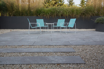Moderne Gestaltung im Materialmix: Stühle und Tisch auf einer Terrasse aus Naturstein Platten...