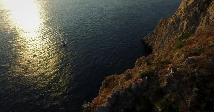 Pan right, boat approaching Faraglioni Arch at sunset