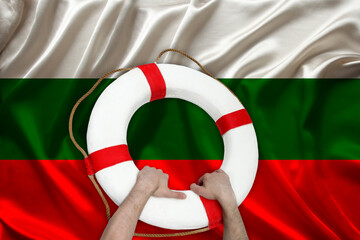 male hands hold on a white life buoy on the background of the silk national flag of the country...