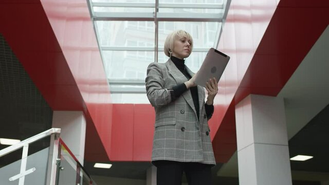 A bottom view slow motion close up shot of a blonde business woman in a grey overcoat using a tablet to keep in touch with her colleagues