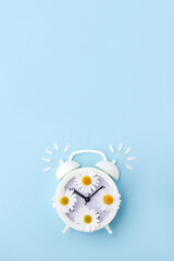 Alarm clock decorated with flowers of chamomile on light blue background. New day start concept. Empty place for inspirational, motivational text or quote. Selective focus